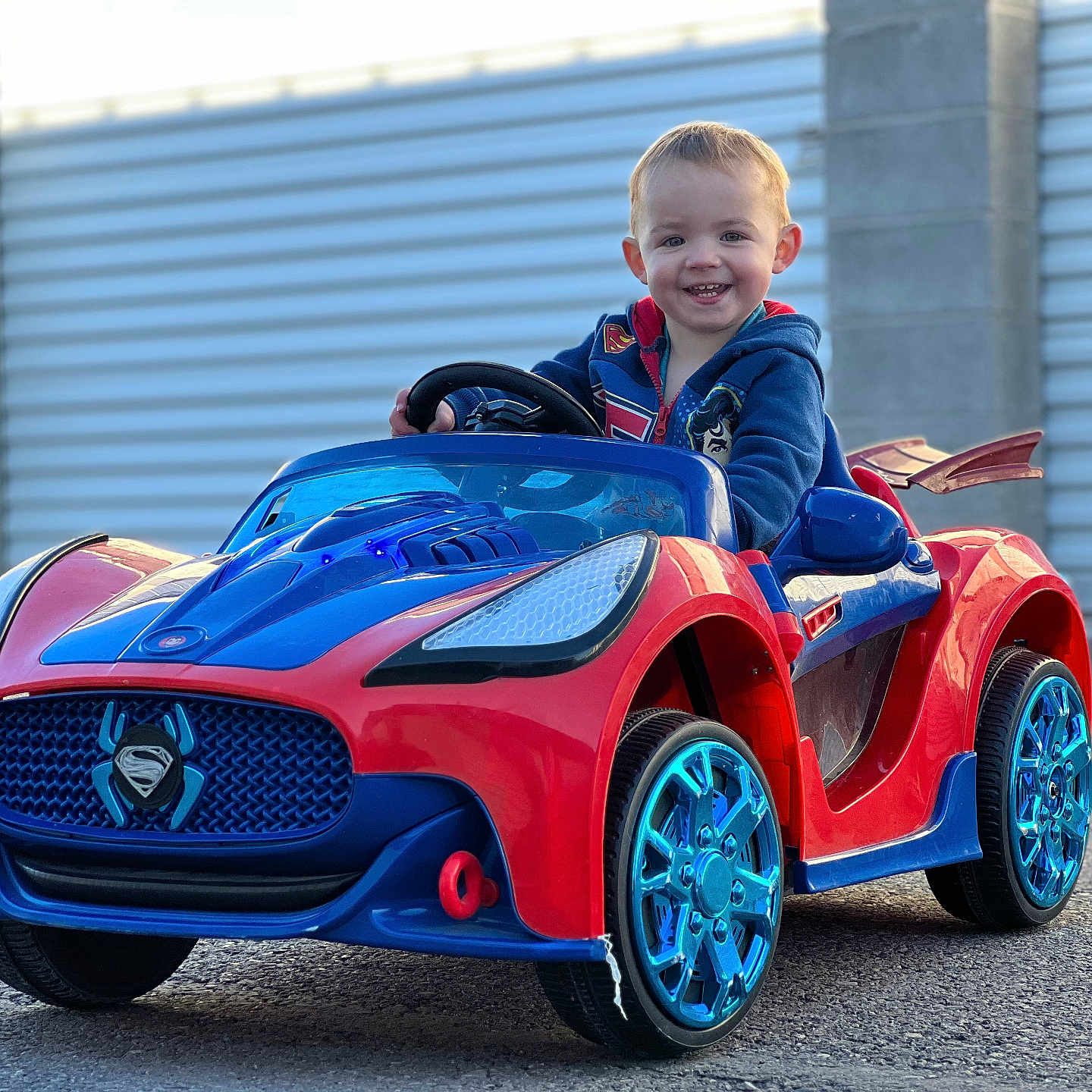 William joined the competition — help win amazing prizes! blue, casual, child, daylight, fun, happy, hoodie, outdoor, pavement, person, play, red, small_child, smiling, superhero, toddler, toy_car, vehicle, wheels, young
