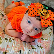 Joy is registered to the contest to win money with this photo: baby, infant, newborn, blue_eyes, orange_outfit, polka_dot_bow, halloween_bow, headband, pumpkin_decor, floral_pillow, cushion, closeup, portrait, lying_down, hands_together, cute, soft_lighting, warm_colors, fabric_pattern, props