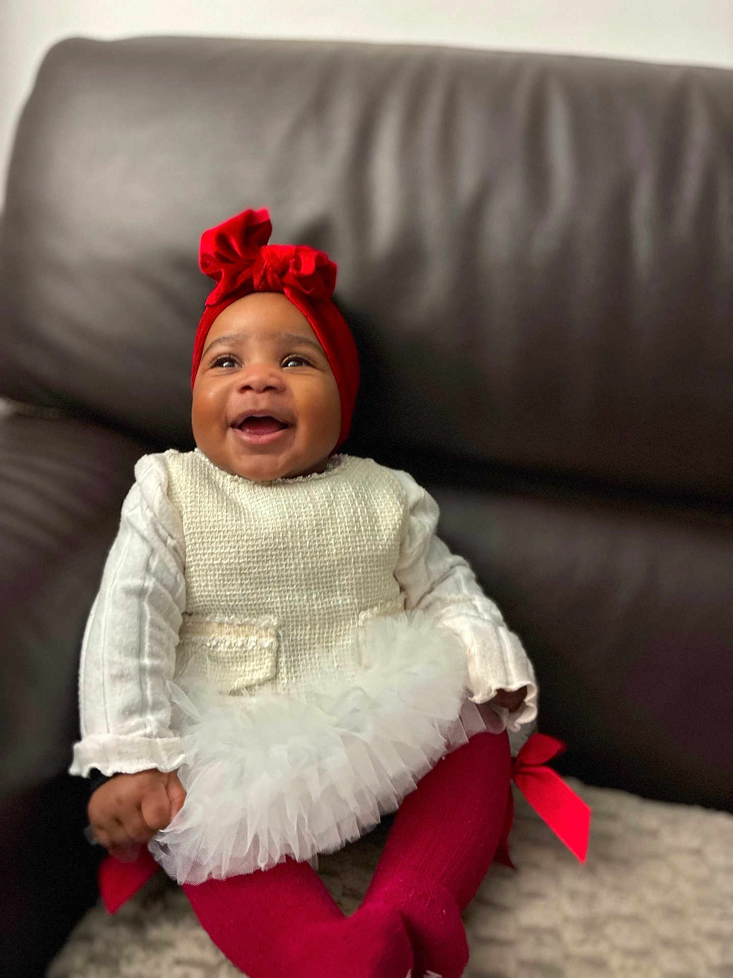 Anayah a rejoint le concours — aidez-le/la à gagner de superbes lots ! baby, child, smiling, red_headband, white_outfit, tutu, red_tights, sitting, couch, leather, happy, portrait, indoor, cute, toddler, clothing, headwear, fashion, cozy, infant