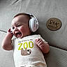 baby, infant, headphones, smiling, couch, onesie, clothing, sloth, wooden_plaque, milestone, six_months, happy, portrait, indoor, child, cute, lying_down, face, expression, celebration