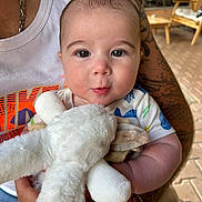Rafaël participe au concours pour gagner de l'argent avec cette photo : baby, child, infant, stuffed_animal, toy, tattoo, arm, person, white_tank_top, indoor, furniture, wooden_chair, cute, closeup, holding, smiling, face, eyes, skin, soft_toy