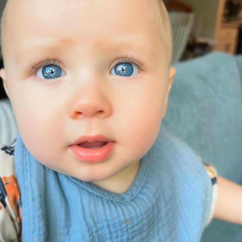 Edward Eible is registered to the contest to win money with this photo: baby, bib, blue_eyes, child, close_up, clothing, curious, cute, expression, face, head, indoor, infant, light_hair, person, portrait, skin, soft_texture, toddler, young_child