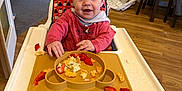 Iris is registered to the contest to win money with this photo: baby, child, feeding, food, footwearless, furniture, happy, high_chair, home, indoor, kitchen, messy, person, plate, red_clothing, scrambled_eggs, smiling, strawberries, table, wood_floor