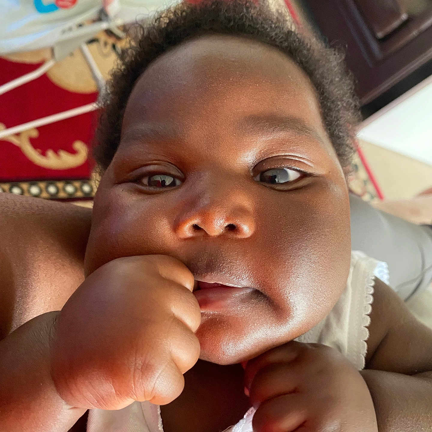 Gina is registered to the contest to win money with this photo: baby, cheeks, child, close_up, colorful, curious, cute, expression, face, fist, hand, home, indoor, infant, person, portrait, skin, toy, white_clothing, young