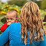 baby, child, person, adult, hair, blonde, curly_hair, blue_shirt, red_clothing, outdoor, nature, sunflower, greenery, portrait, holding, back_view, face, expression, young_child, daylight