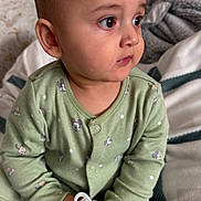 Azaan joined the competition — help win amazing prizes! baby, child, pacifier, green_pajamas, mickey_mouse, sitting, blanket, indoor, cute, face, portrait, infant, hands, expression, looking_away, cozy, soft_lighting, young_child, clothing, bedroom