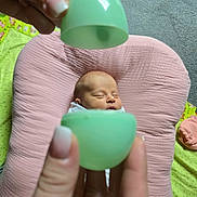 Ila is registered to the contest to win money with this photo: baby, newborn, infant, sleeping, pink_cushion, green_egg, hands, fingers, carpet, blanket, soft, cozy, cute, portrait, closeup, indoor, peaceful, child, person, resting