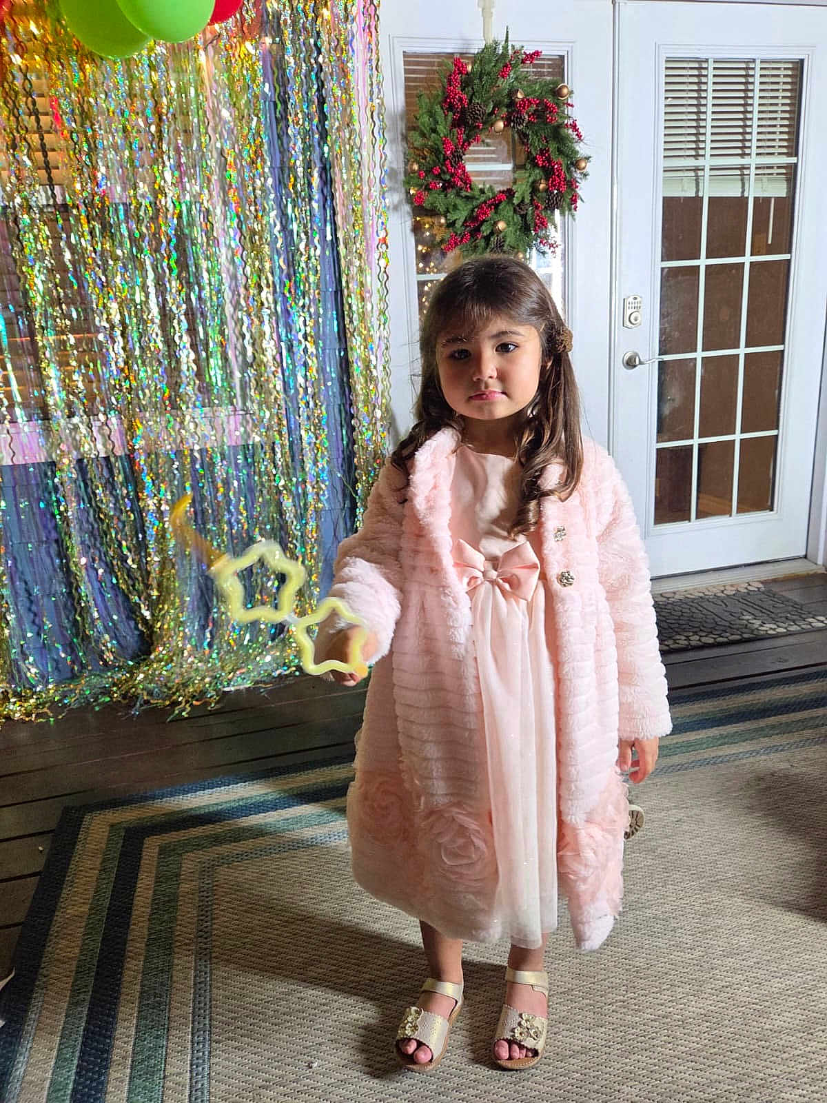 Brianna is registered to the contest to win money with this photo: child, girl, pink_dress, coat, party_decor, wreath, balloons, sparkly_backdrop, door, rug, sandals, portrait, standing, bubble_wand, indoor, curly_hair, festive, wooden_floor, carpet, expression