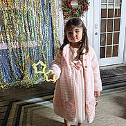 Brianna is registered to the contest to win money with this photo: balloons, child, door, dress, face, girl, hair, holiday_decor, indoor, party, pink_coat, portrait, rug, sandals, serious_expression, sparkly_backdrop, star_wand, tinsel, wooden_floor, wreath