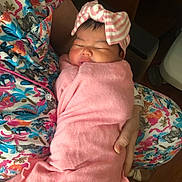 Brianna is registered to the contest to win money with this photo: baby, newborn, swaddle, pink, bow, sleeping, infant, parent_arm, patterned_clothing, hospital_bracelet, cozy, cute, holding, portrait, indoor, soft_fabric, peaceful, wrap, nap, head