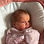 newborn, baby, infant, pink_blanket, floral_onesie, face, expression, cushion, baby_seat, sleepwear, soft_texture, indoors, close_up, cute, small_hands, wrapped, resting, child, portrait, cozy