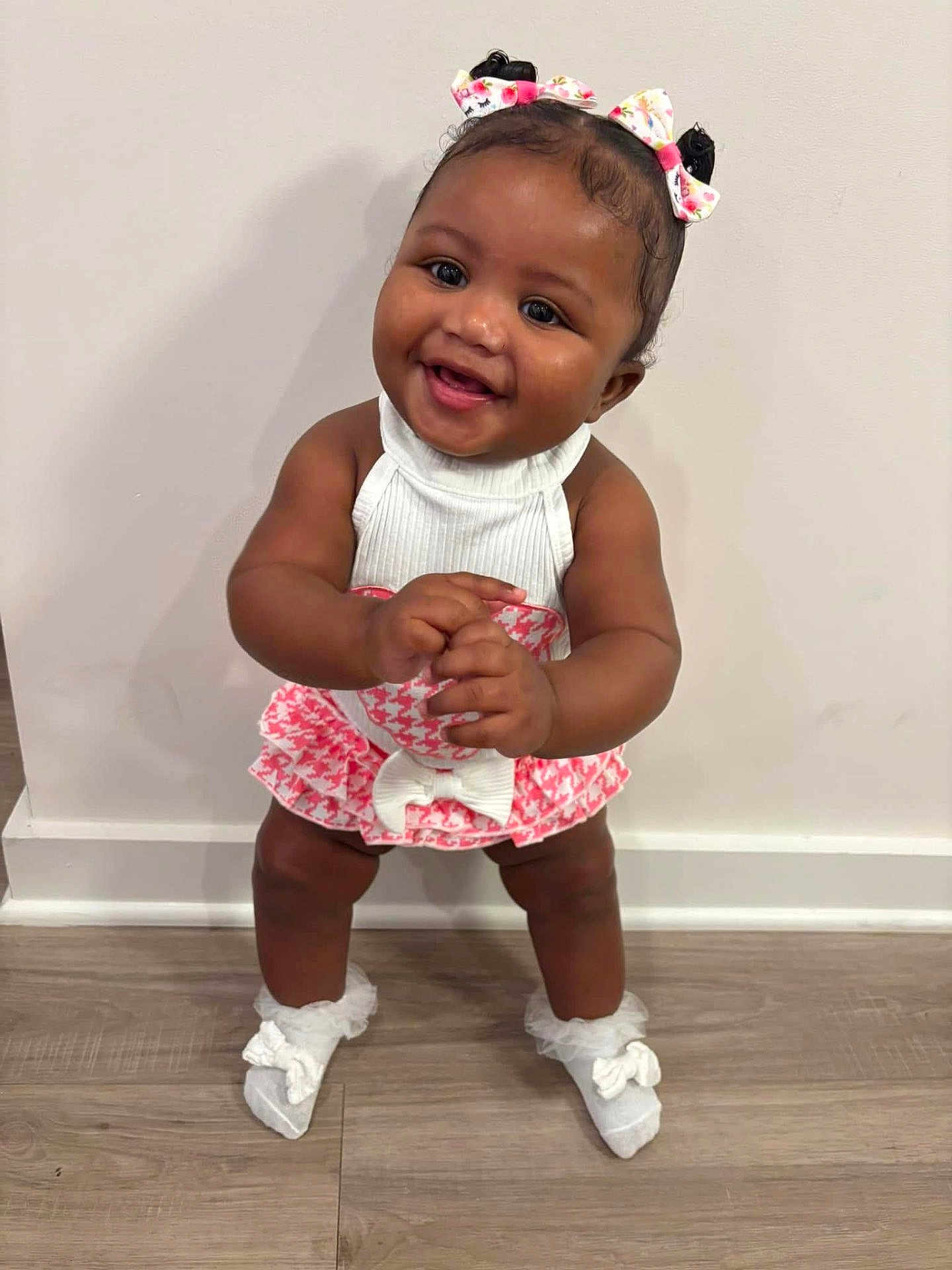 Khalani joined the competition — help win amazing prizes! baby, child, smiling, standing, white_socks, bows, pink_dress, white_top, floor, wooden_floor, indoor, happy, cute, person, portrait, toddler, hair_bows, skin, hands, feet