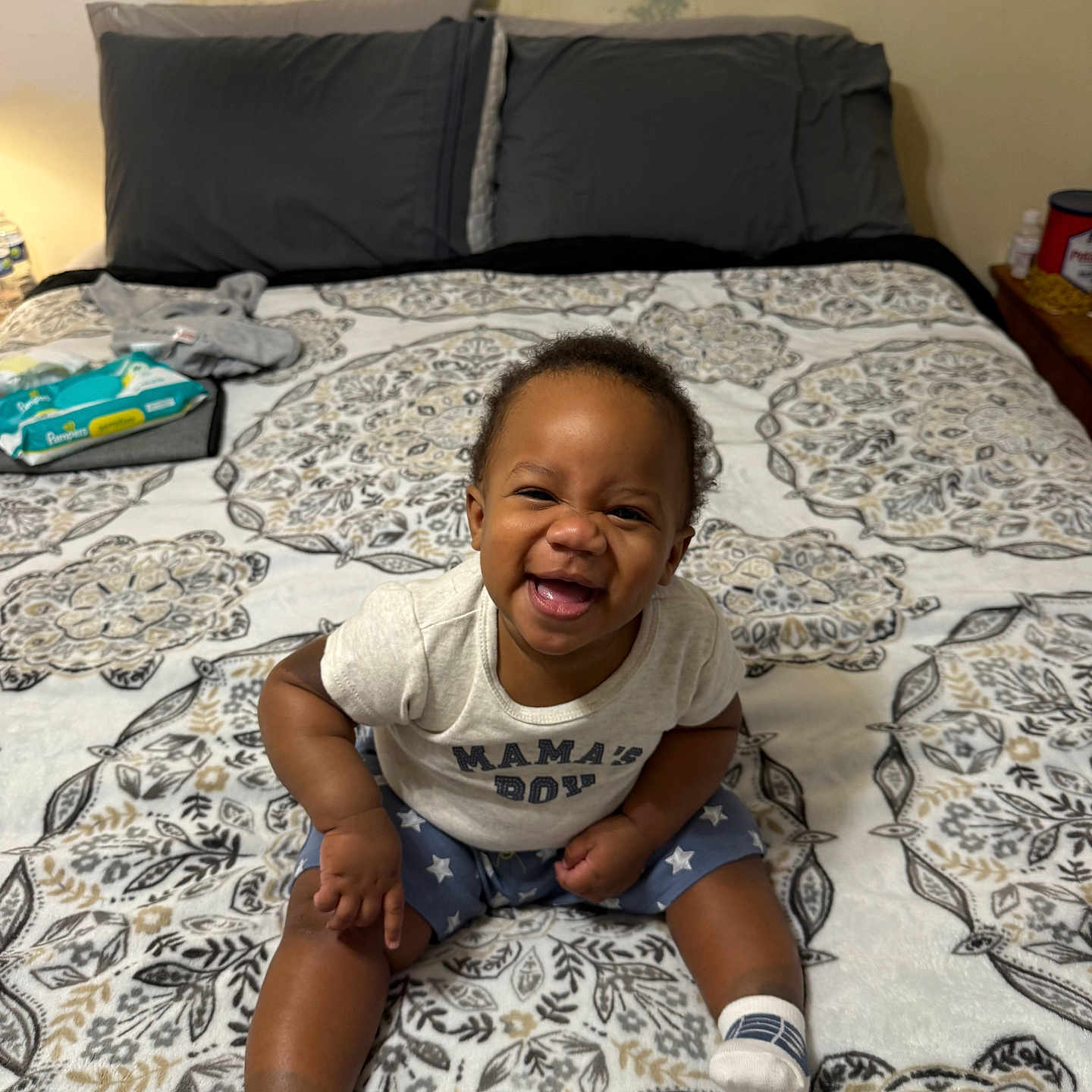 Christian is registered to the contest to win money with this photo: baby, bed, blanket, child, clothing, face, furniture, happy, indoor, infant, joyful, pattern, person, pillow, room, sitting, smiling, socks, text_on_clothing, toddler