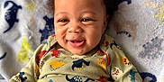 Saint joined the competition — help win amazing prizes! baby, smiling, curly_hair, dinosaur_pattern, onesie, blanket, infant, happy, child, cute, lying_down, indoors, portrait, apparel, toddler, face, skin, playful, cozy, soft