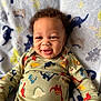 baby, smiling, curly_hair, dinosaur_pattern, onesie, blanket, infant, happy, child, cute, lying_down, indoors, portrait, apparel, toddler, face, skin, playful, cozy, soft