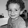 Liam participe au concours pour gagner de l'argent avec cette photo : toddler, child, curly_hair, smile, indoor, portrait, dinosaur_shirt, table, wooden_surface, modern_interior, computer, decor, face, person, long_sleeve_shirt, happy, cute, young_child, black_and_white, casual