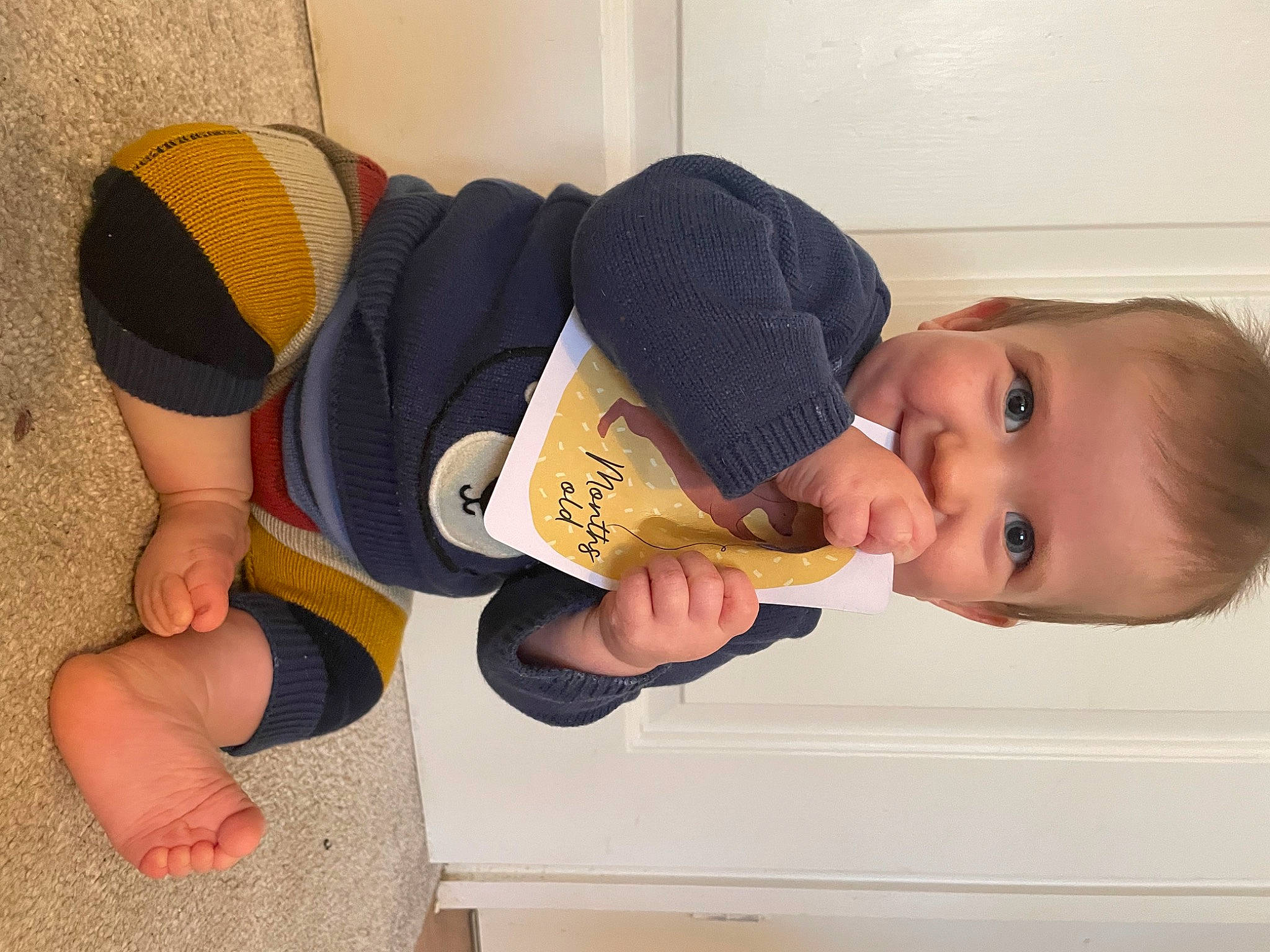 Henry is registered to the contest to win money with this photo: arm, baby_toddler_clothing, comfort, elbow, finger, flooring, gesture, headgear, human_body, human_leg, joint, knee, leg, neck, person, sleeve, smile, sportswear, thigh, thumb