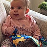 Gabriella joined the competition — help win amazing prizes! baby, child, indoors, couch, pink_clothing, patterned_pants, book, colorful, curious, seated, hand, face, blue_eyes, short_hair, toy, home, cozy, playful, infant, smiling