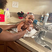 Zymir is registered to the contest to win money with this photo: baby, bath, sink, bubbles, foam, soap, kitchen, child, person, arms, water, cleaning, smile, happy, head, cabinet, countertop, bottle, mickey_mouse, playful