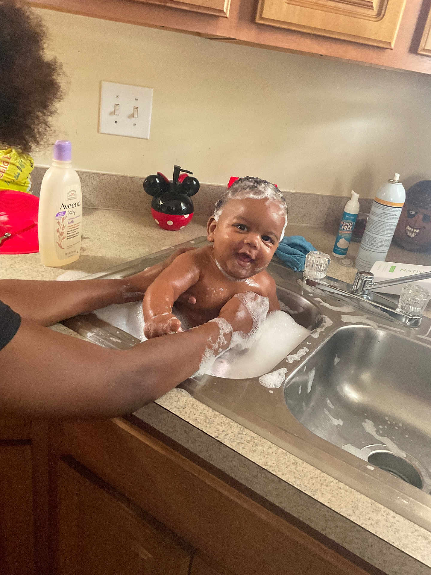 Zymir is registered to the contest to win money with this photo: baby, bath, sink, bubbles, foam, soap, kitchen, child, person, arms, water, cleaning, smile, happy, head, cabinet, countertop, bottle, mickey_mouse, playful