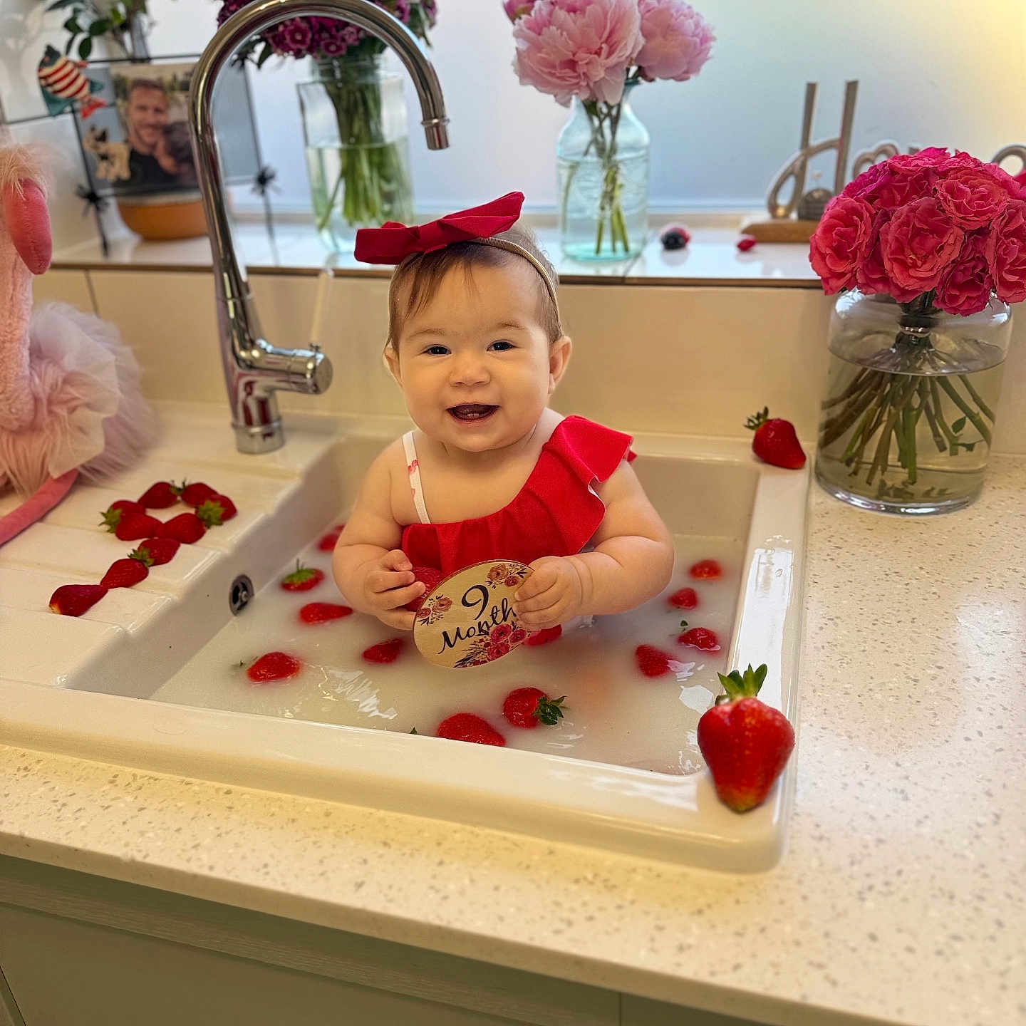 Olivia joined the competition — help win amazing prizes! baby, child, countertop, cute, flowers, happy, indoor, kitchen, milestone, milky_water, person, plush_toy, portrait, red_bow, red_outfit, sink, smiling, strawberries, vase, water