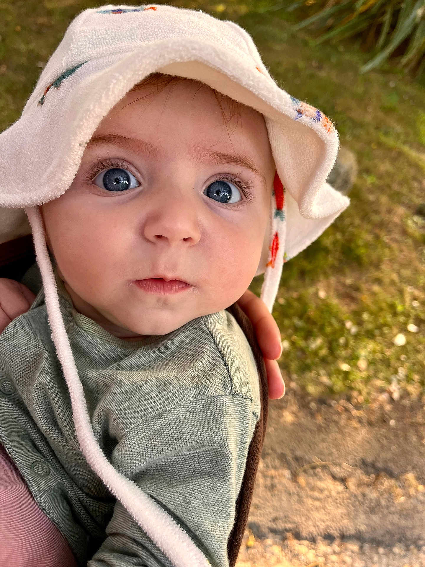 Théo a rejoint le concours — aidez-le/la à gagner de superbes lots ! baby, child, face, hat, blue_eyes, curious, outdoor, person, portrait, clothing, hand, skin, cute, infant, looking, headwear, green_clothing, daylight, nature, closeup