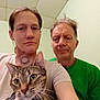 Twiggy is registered to the contest to win money with this photo: adult, animal, casual, cat, ceiling, closeup, face, green_shirt, holding, indoor, light_skin, looking, people, person, pet, portrait, room, short_hair, tabby_cat, whiskers