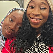 Amari is registered to the contest to win money with this photo: two_people, smiling, portrait, close_up, indoor, headband, braided_hair, patterned_clothing, warm_lighting, happy, friendly, casual, young_person, person, face, head_and_shoulders, female, black_hair, colorful_hair, cozy