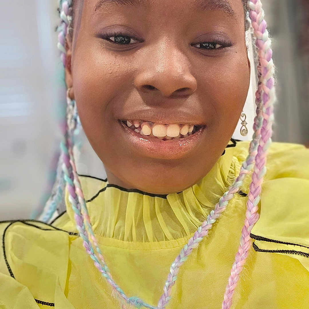 Amari is registered to the contest to win money with this photo: braided_hair, casual, child, closeup, cute, earrings, face, fashion, hairstyle, happy, indoor, joyful, pastel_colors, person, portrait, ruffles, skin, smiling, yellow_clothing, young_person