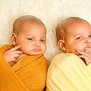Amaya And Ariana joined the competition — help win amazing prizes! baby, infant, swaddled, blanket, yellow_blanket, orange_blanket, cute, portrait, face, expression, skin, head, lying_down, indoor, soft_texture, toddler, child, newborn, two_babies, closeup