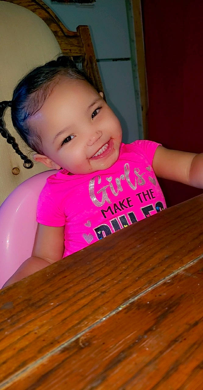 Armani is registered to the contest to win money with this photo: baby, baby_toddler_clothing, cheek, child, chin, desk, eyelash, finger, hairstyle, happy, iris, joy, lip, magenta, nose, person, pink, skin, smile, table