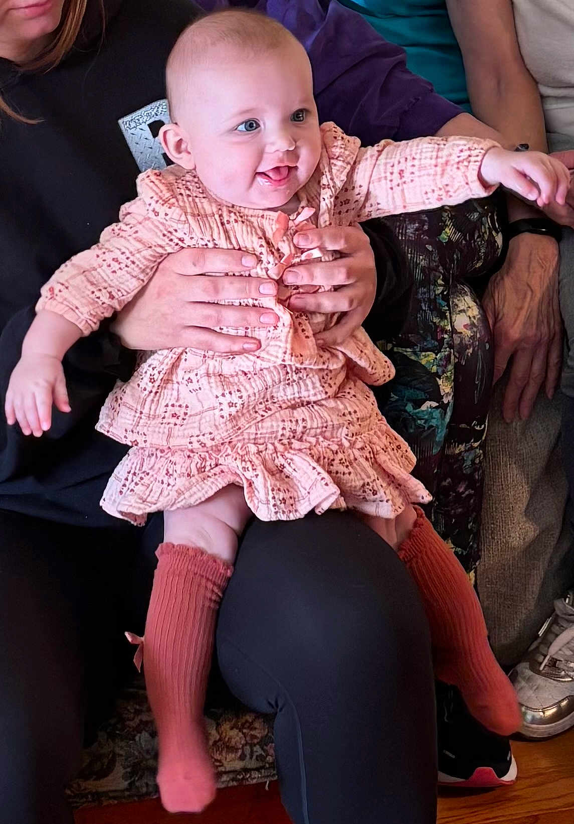 Darla is registered to the contest to win money with this photo: baby, child, person, infant, holding_hands, dress, socks, happy, tongue_out, indoor, seated, adult_hands, furniture, couch, clothing, smiling, cute, legs, face, human