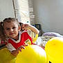 Maddie joined the competition — help win amazing prizes! child, girl, balloons, yellow, pigtails, red_shirt, window_blind, bed, pillow, blanket, indoor, smiling, playful, hand, face, hair, light, room, casual_clothing, young