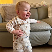 Eli-James is registered to the contest to win money with this photo: baby, blue_eyes, candid, cheeks, couch, hand, hardwood_floor, home_interior, infant, living_room, overalls, plush_cushion, portrait, smiling, soft_light, standing, striped_shirt, teeth, toddler, winnie_the_pooh_print