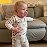 baby, blue_eyes, candid, cheeks, couch, hand, hardwood_floor, home_interior, infant, living_room, overalls, plush_cushion, portrait, smiling, soft_light, standing, striped_shirt, teeth, toddler, winnie_the_pooh_print