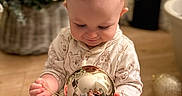 Eli-James is registered to the contest to win money with this photo: baby, bauble, bokeh, child, christmas_ornament, christmas_tree, close_up, cozy, decorations, festive, hands, holiday_lights, indoor, infant, pajamas, reflection, sitting, smiling, toy_elf, wooden_floor