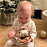 baby, bauble, bokeh, child, christmas_ornament, christmas_tree, close_up, cozy, decorations, festive, hands, holiday_lights, indoor, infant, pajamas, reflection, sitting, smiling, toy_elf, wooden_floor