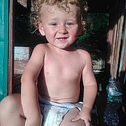 Douglas joined the competition — help win amazing prizes! toddler, child, curly_hair, diaper, smile, pointing, sunlight, wooden_structure, water_bottle, outdoor, skin, bare_chest, playful, young_child, person, face, sitting, cute, daylight, expression