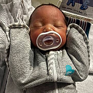 Sincere is registered to the contest to win money with this photo: newborn, baby, sleeping, pacifier, grey_clothing, blanket, hospital, infant, face, hands, cozy, cute, child, portrait, zipped_jacket, peaceful, indoors, soft, resting, young