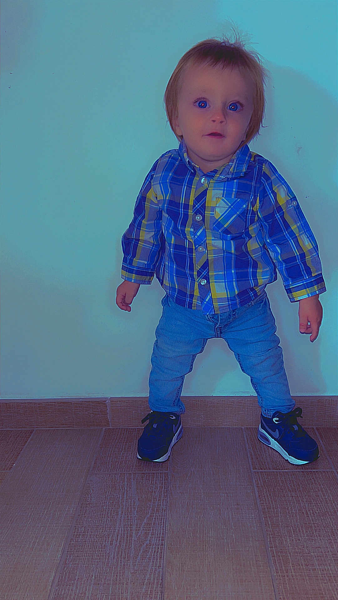 Ezio participe au concours pour gagner de l'argent avec cette photo : toddler, child, plaid_shirt, jeans, sneakers, standing, indoor, wooden_floor, curious_expression, casual_clothing, short_hair, blue_eyes, wall, flooring, portrait, person, young_child, cute, small_hands, footwear