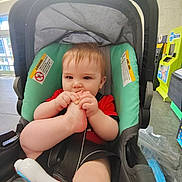 Liam joined the competition — help win amazing prizes! baby, child, stroller, foot, chewing, red_shirt, seatbelt, indoor, store, toy, plastic_bag, floor, window, warning_label, curious, infant, cute, playful, person, young_child