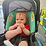 baby, child, stroller, foot, chewing, red_shirt, seatbelt, indoor, store, toy, plastic_bag, floor, window, warning_label, curious, infant, cute, playful, person, young_child