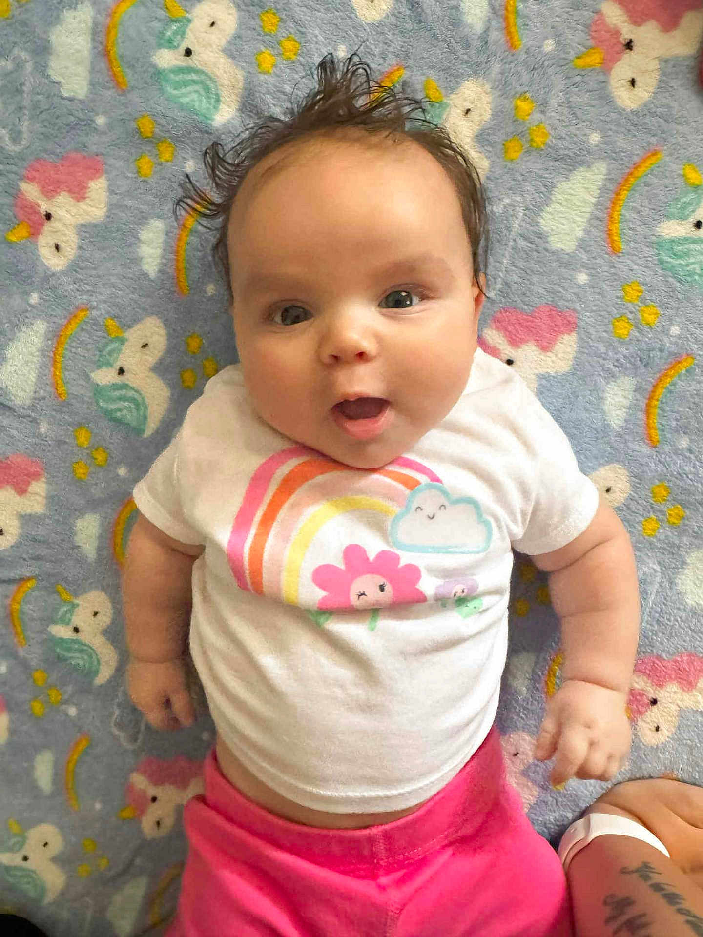 Jayleigh is registered to the contest to win money with this photo: baby, infant, child, person, smiling, cute, lying_down, blanket, unicorn, rainbow, clothing, tshirt, pink_pants, happy, face, hair, expression, indoors, colorful, soft