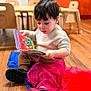 toddler, child, reading, book, floor, wooden_floor, indoor, furniture, chair, table, colorful, fabric, red, blue, clothing, sitting, curly_hair, casual, concentration, young_child