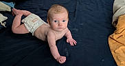 áine is registered to the contest to win money with this photo: baby, infant, diaper, blue_eyes, lying_down, blanket, pillow, indoor, curious, child, skin, young, sleeping_area, cozy, toddler, face, person, resting, cute, expression
