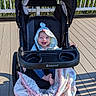 áine joined the competition — help win amazing prizes! baby, stroller, blanket, hooded_clothing, outdoor, deck, sunlight, happy, smiling, infant, babytrend, wooden_floor, greenery, nature, child, seat, footwear, person, portrait, daylight