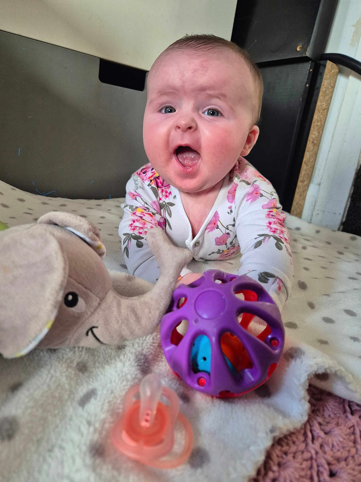 Oliwia joined the competition — help win amazing prizes! baby, child, infant, toy, stuffed_animal, elephant, ball, pacifier, blanket, polka_dot, floral_clothing, onesie, expression, indoor, carpet, face, hands, playing, cute, happy
