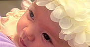 Ava is registered to the contest to win money with this photo: baby, infant, flower_headband, close_up, portrait, child, cute, looking_away, soft_lighting, person, face, skin, clothing, hand, holding, young_child, indoors, headwear, gentle, curious