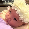 baby, infant, flower_headband, close_up, portrait, child, cute, looking_away, soft_lighting, person, face, skin, clothing, hand, holding, young_child, indoors, headwear, gentle, curious