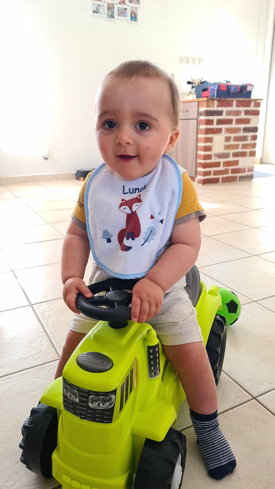 Lubin participe au concours pour gagner de l'argent avec cette photo : automotive_design, baby, baby_products, baby_toddler_clothing, child, cleanliness, floor, flooring, fun, happy, human_leg, knee, person, riding_toy, shorts, smile, t_shirt, tire, toddler, vehicle